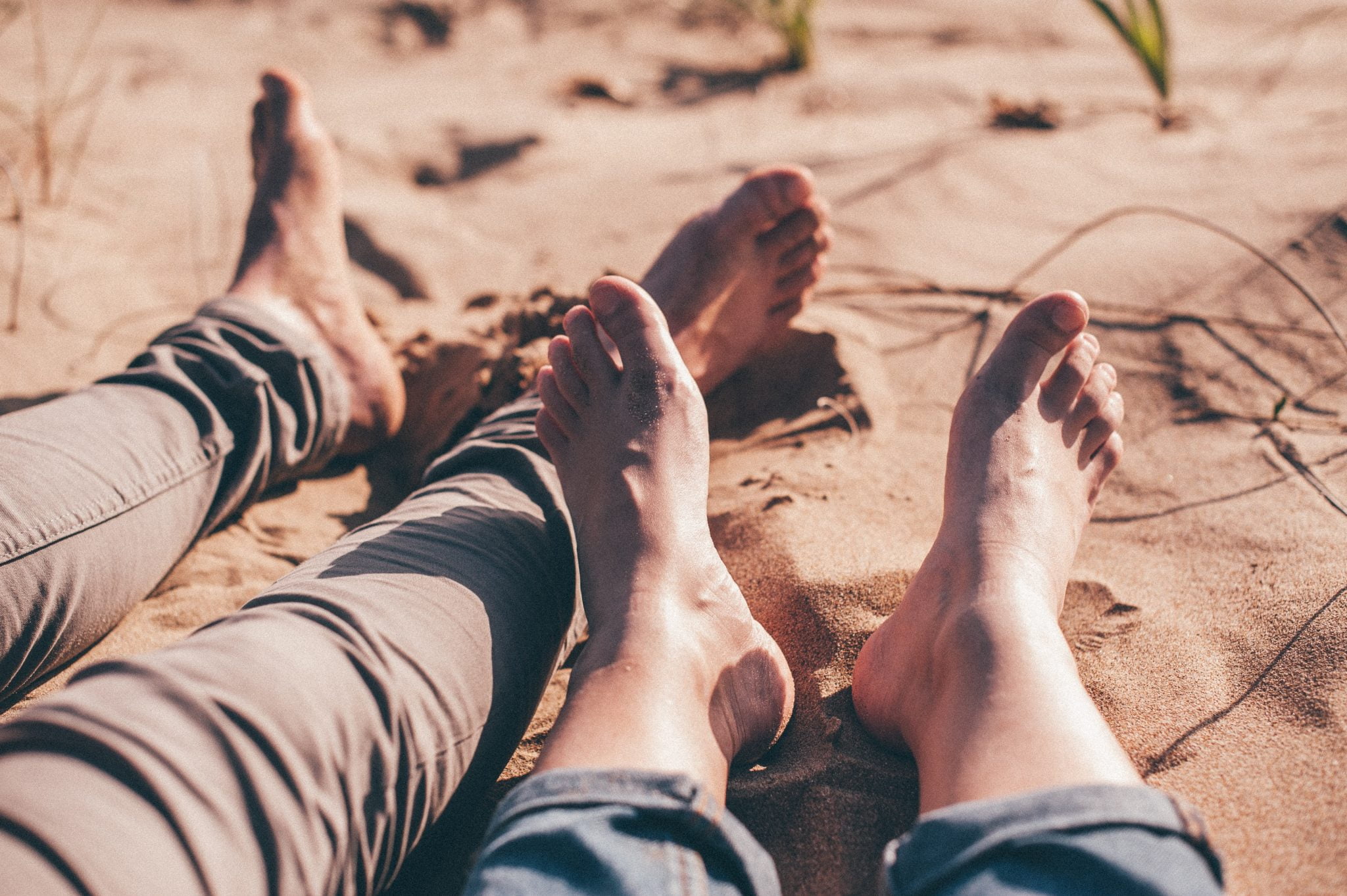 Two pairs of feet on a beach with sandy toes